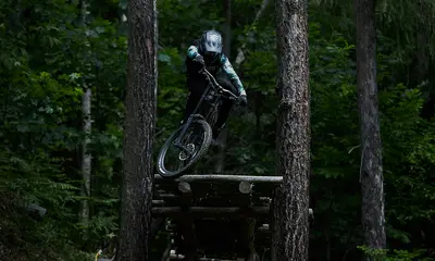 Ab Dezember 2026: glockna – das wohl coolste Hotel in Fusch Mountainbiker springt mit Helm und Schutzkleidung zwischen Bäumen im Wald