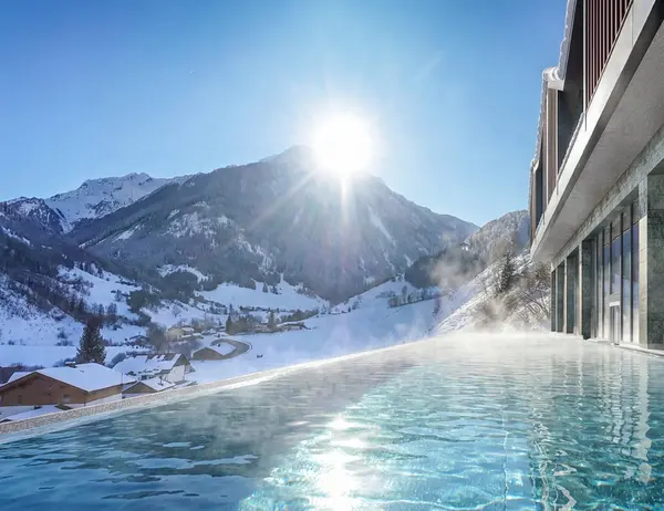 Ab Dezember 2026: glockna – das wohl coolste Hotel in Fusch Infinity-Pool mit Bergblick und Sonnenschein in verschneiter Winterlandschaft